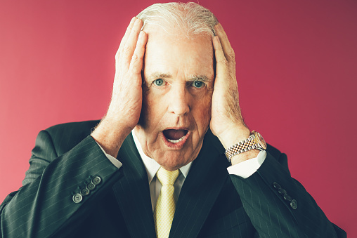 Closeup portrait of shocked senior business man clutching head with his mouth open. Isolated front view on purple background.