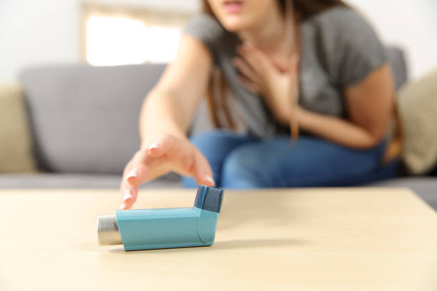 Girl suffering asthma attack reaching inhaler Girl suffering asthma attack reaching inhaler sitting on a couch in the living room at home asthmatic stock pictures, royalty-free photos & images