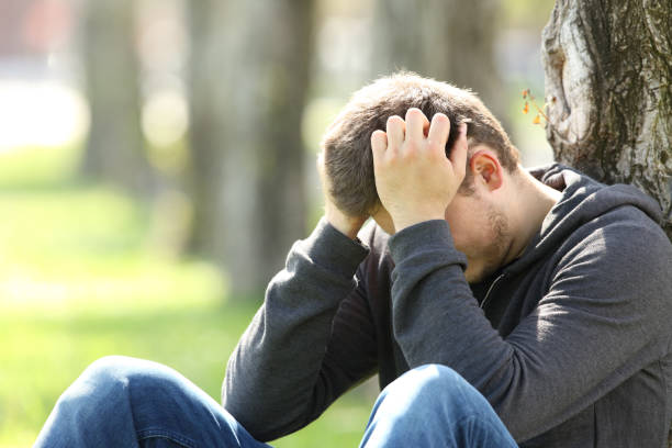 Sad teen lamenting in a park Portrait of a single sad teen lamenting sitting on the grass in a park low self esteem stock pictures, royalty-free photos & images