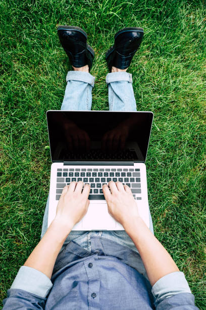 istock Cropped shot of man using laptop with blank screen while sitting on green grass 811355404