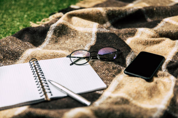 close up view of blank notebook, smartphone and eyeglasses on blanket