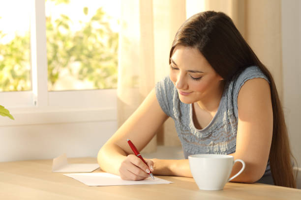 girl writing a letter on a table - writing letter correspondence women imagens e fotografias de stock