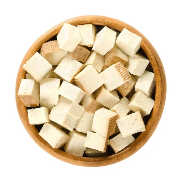 Smoked tofu cubes in wooden bowl. Bean curd. Coagulated soy milk, pressed into firm white blocks. Component of Asian cuisine. Meat substitute. Isolated macro food photo close up from above over white