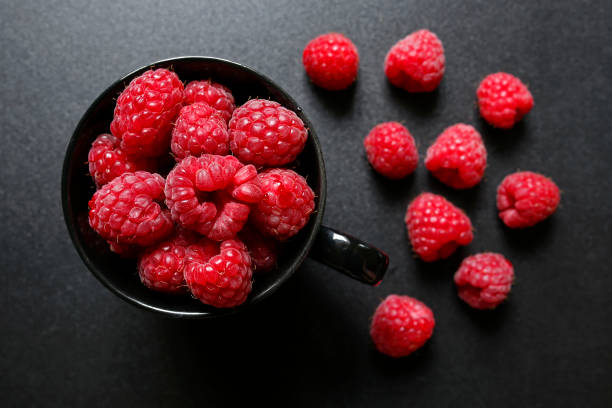istock fresh raspberries in a cup on black background 811380576