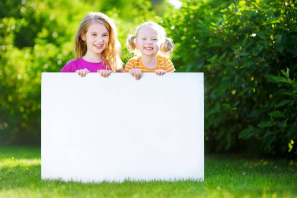 two cute little sisters holding big blank whiteboard - preschooler portrait family outdoors imagens e fotografias de stock