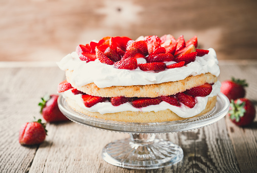 Strawberry and cream sponge cake on glass stand. Homemade summer dessert on wooden rustic table