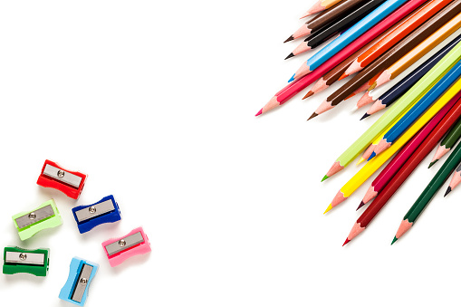 Large group of multi colored pencils and six multi colored plastic pencil sharpeners shot from above on white background. The pencils are coming from the top-right corner and the sharpeners and shavings are at the bottom-left corner of an horizontal frame leaving useful copy space for text and/or logo at the center. DSRL studio photo taken with Canon EOS 5D Mk II and Canon EF 100mm f/2.8L Macro IS USM