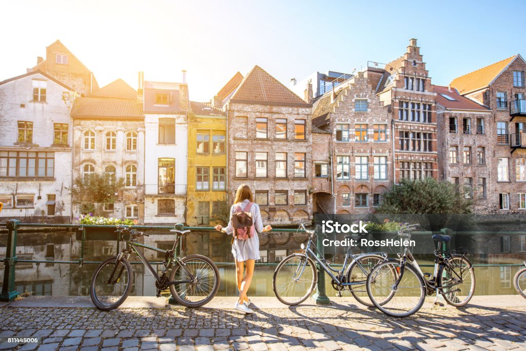 Woman traveling in Gent old town, Belgium Sunrise view on the water channel with beautiful old buildings with woman standing near the bicycles in Gent city Europe Stock Photo