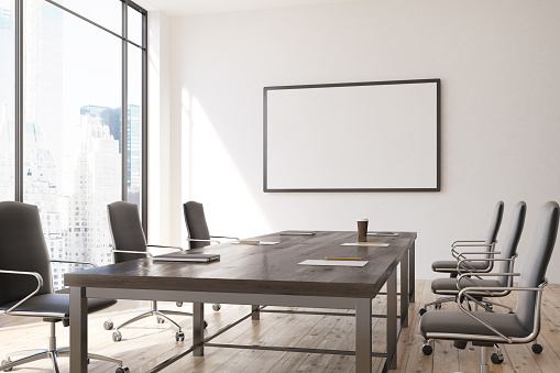 Conference room interior with a framed horizontal poster hanging above a long wooden table with office chairs around it. 3d rendering mock up