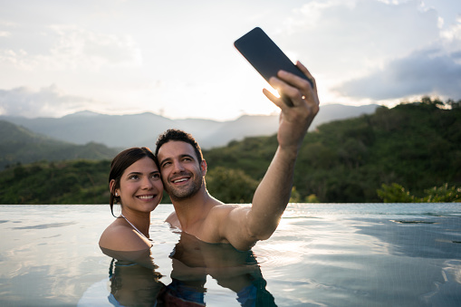 Happy couple on vacations taking a selfie in the swimming pool - lifestyle concepts