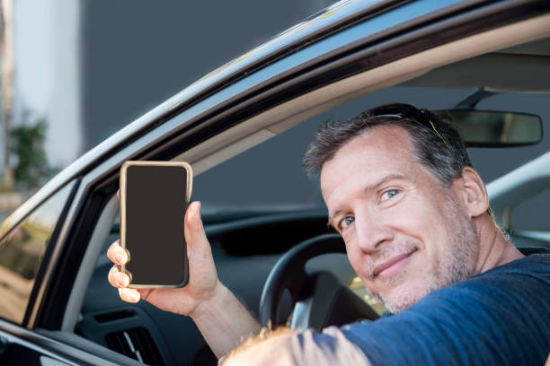 istock Mature Driver Picking up Passenger Shows Mobile Phone to Camera 811459518