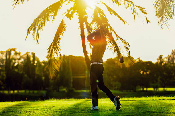 homem asiático a jogar golfe em um campo de golfe contra o pôr do sol - golf golf swing men exercising - fotografias e filmes do acervo
