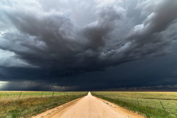 Dark storm clouds over a dirt road Dark storm clouds sky background with a straight dirt road. dramatic sky stock pictures, royalty-free photos & images