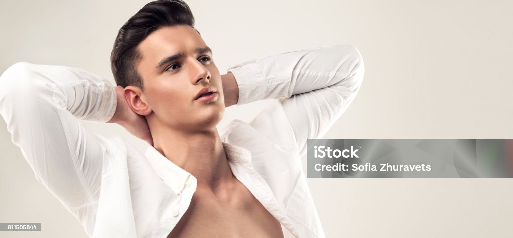 Handsome man with trendy hairstyle dressed in a unbuttoned white shirt. Fashion portrait of a handsome man with trendy hairstyle dressed in a unbuttoned white shirt with dreaming look. Symbol of desire to have perfect vacation and relaxation. Men Stock Photo