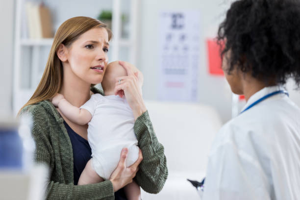 Concerned mom talks with doctor about baby's health Worried new mom comforts her newborn baby while talking with the child's pediatrician. worried mom with kids stock pictures, royalty-free photos & images