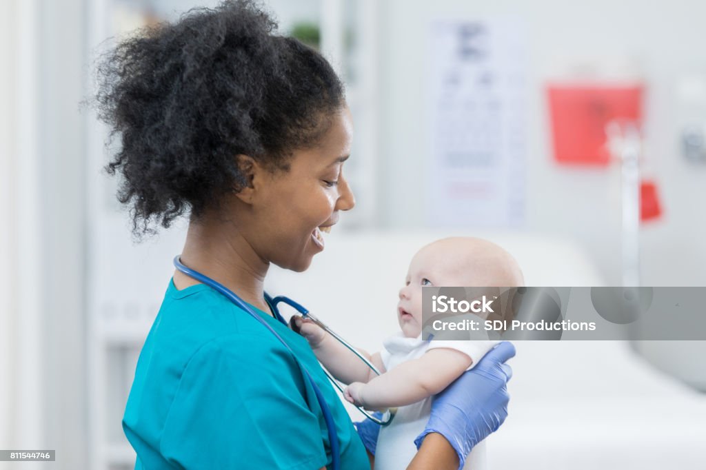 Adorable baby girl looks at caring nurse Sweet baby girl looks up at a caring pediatrician during a well check appointment. The doctor is holding the baby. Baby - Human Age Stock Photo