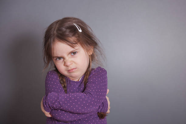 Sulking Girl A little cute Girl is sulking. She is wearing a purple shirt in front of a gray background. puckering stock pictures, royalty-free photos & images