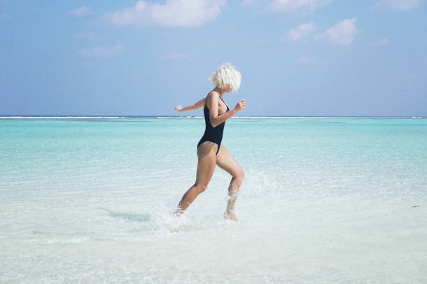 Woman in bikini running through water on sandy beach, Maldives