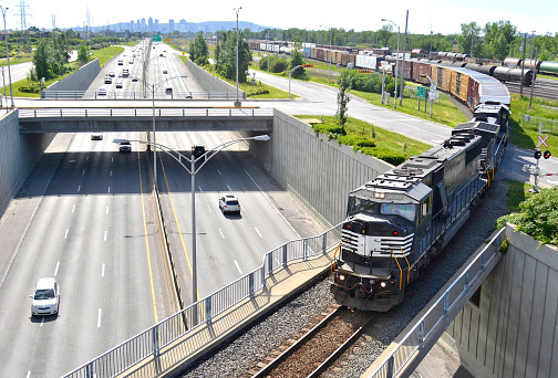 A freight train lumbers across an overpass with car traffic below.