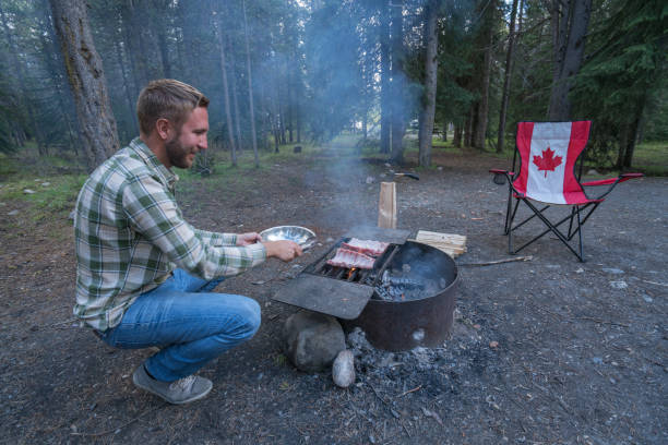 View of a young man cooking food on fire pit barbecue in Canada.