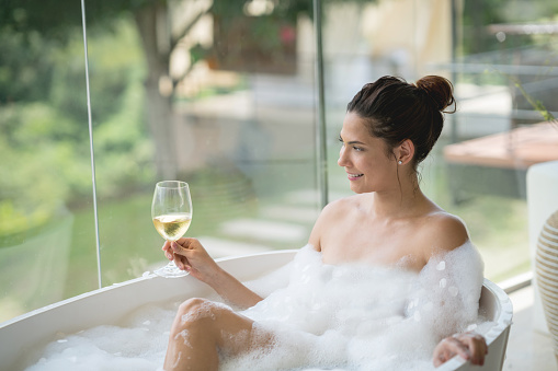Beautiful woman taking a bath at home and drinking a glass of wine while relaxing - lifestyle concepts