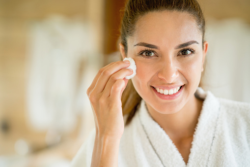 Portrait of a beautiful woman cleansing her face with a cotton bud and looking at the camera smiling - beauty concepts