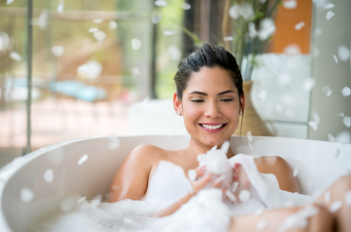 Portrait of a beautiful woman relaxing at home with a bubble bath and foam falling aroung her - lifestyle concepts