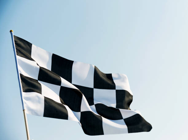 клетчатый флаг, развеваемый на голубом небе - checkered flag flag auto racing starting line стоковые фото и изображения