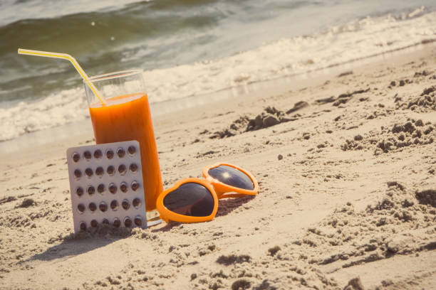 Medical pills, carrot juice and sunglasses at beach, concept of vitamin A and beautiful, lasting tan stock photo