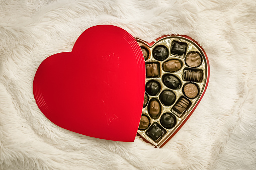 A high-angle view of a heart-shaped box with chocolates on a white fur blanket
