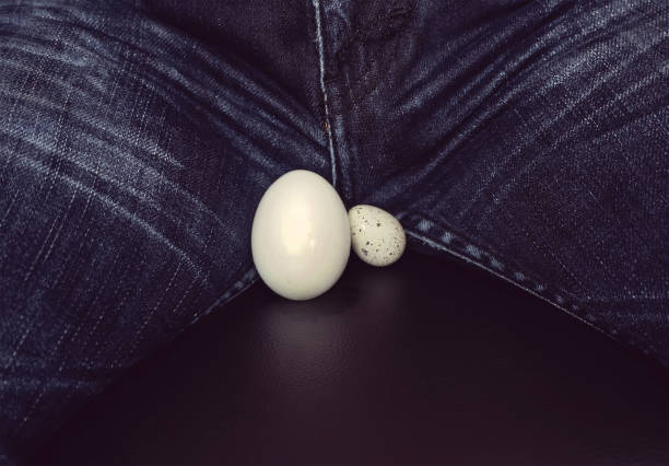 symbol of man's balls two eggs of different sizes between the legs of men. White eggs - a symbol of man's balls testis stock pictures, royalty-free photos & images