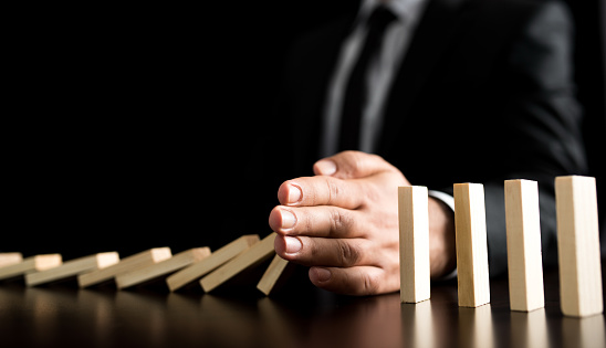 Chain Reaction In Business Concept, Businessman Letting Or Preventing  Dominoes Continuous Toppling On Rustic Wooden Desk