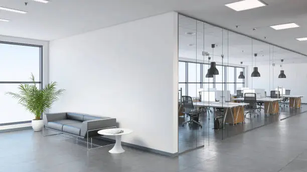 Interior view of a modern office, business template. Left side of the picture is large sofa with a plant and coffee table. Blank wall for copy space. On the right, many office desks with pendant lights above. large windows. gray floor tiles, white walls. Render