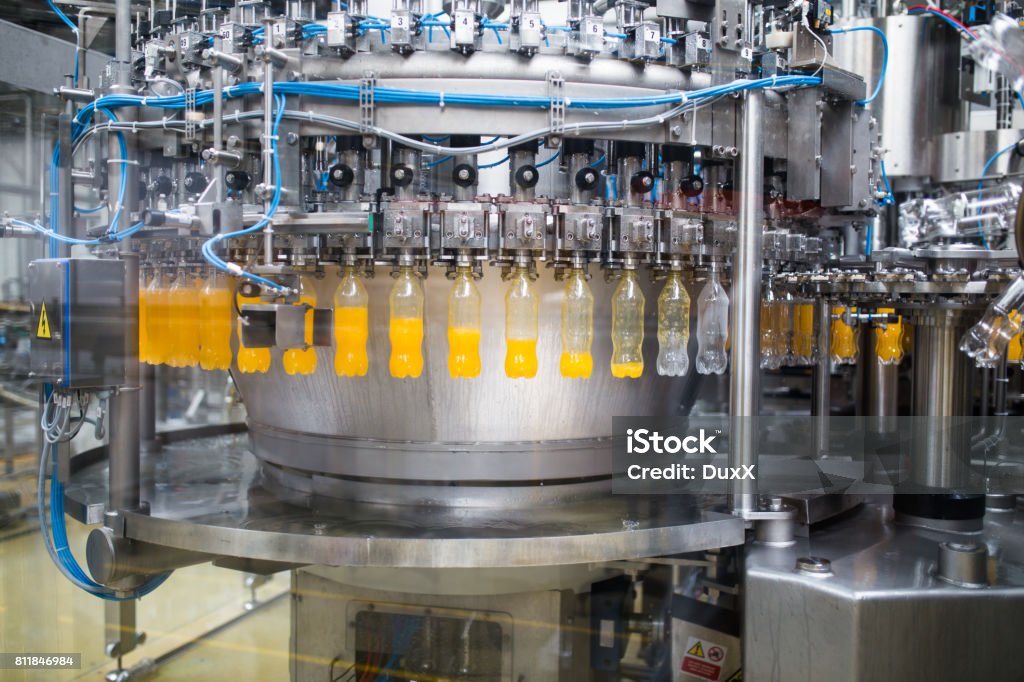 Industrial indoors and machinery Industrial factory indoors and machinery. Robotic factory line for processing and bottling of soda and orange juice bottles. Selective focus. Short depth of field. Factory Stock Photo