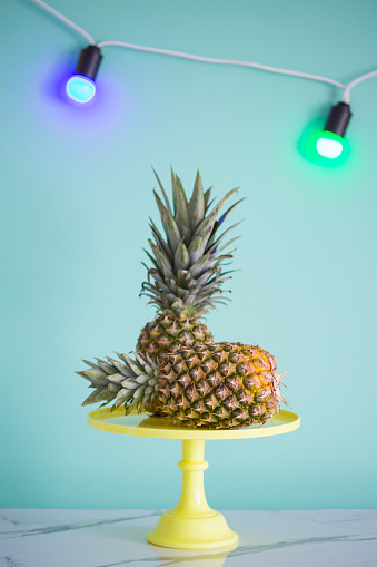 Pineapples on yellow cakestand on the table against colored background.