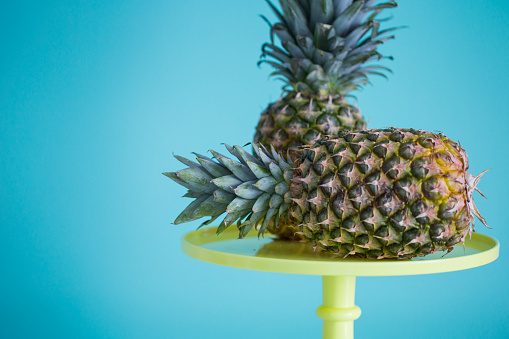 Pineapples on yellow cakestand on the table against colored background.