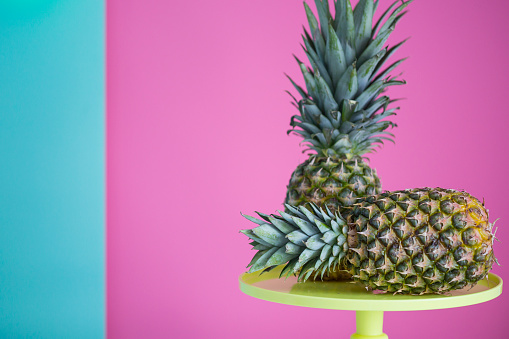 Pineapples on yellow cakestand against colored background.