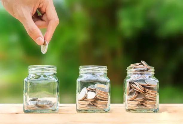 Photo of Conceptual hand putting coins into bottle on nature background,Business investment growth concept