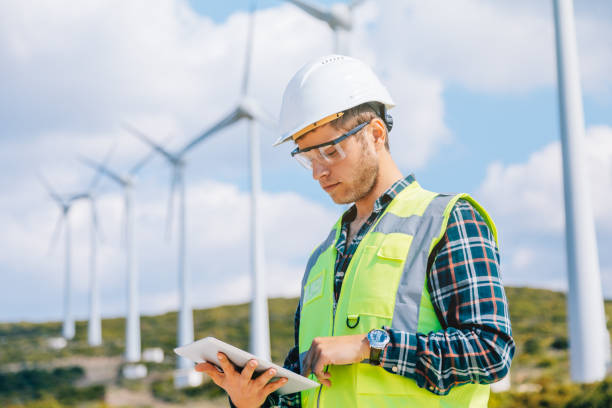 Young engineer man looking and checking wind turbines at field Portrait of young caucasian technician engineer man wearing white worker headwear standing, working, checking farm field system and looking up verify at wind turbine while using digital tablet pc computer for renewable energy plan by wind turbine power generation station in rural landscape. xxxl size field workers stock pictures, royalty-free photos & images