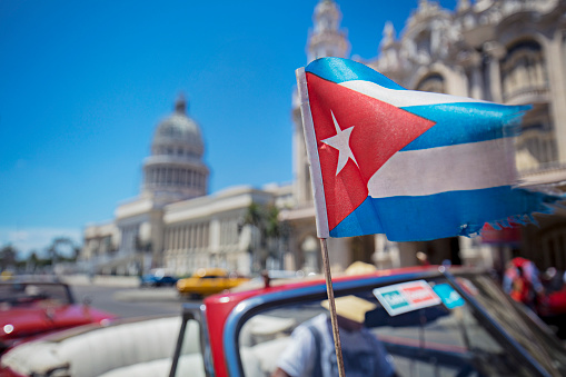 Blurred motion of Cuban flag against Capitolio building in Havana. National flag is in motion against famous parliament building against blue sky. View of travel location in Cuba.