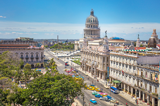Capitolio building by city street against sky. Famous parliament building is in Havana. High angle view of cars and taxis parked on street at historic travel location in Cuba.
