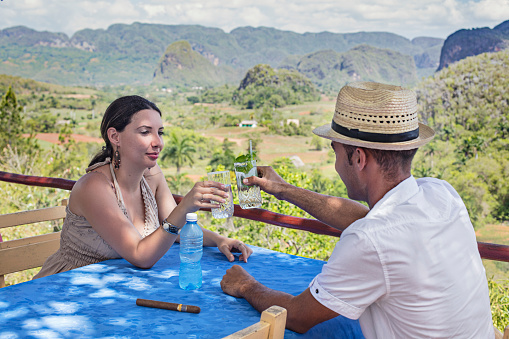 Mid adult couple toasting drinks at outdoor restaurant against Valle De Vinales. Cuban man and woman are enjoying vacation in Cuba. They are wearing casuals.