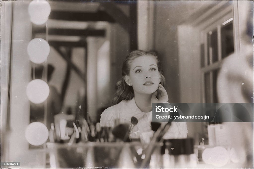 Old 1940s sepia photo of dreamy young woman looking in theater mirror. Retro Style Stock Photo