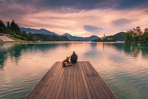Man and dog sitting on wooden deck at Bled lake, Slovenia