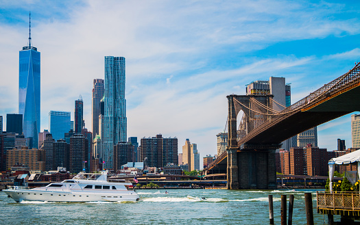 View of Brooklyn Bridge from Harbor with One World Trade Center in background and Yacht sailing down East River in Foreground