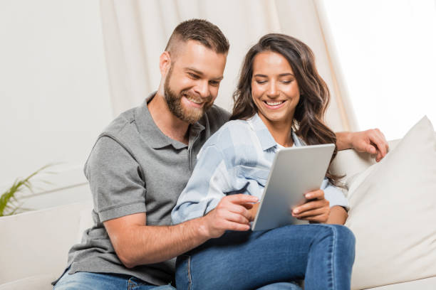 istock young smiling couple using digital tablet while sitting on sofa at home 811967172