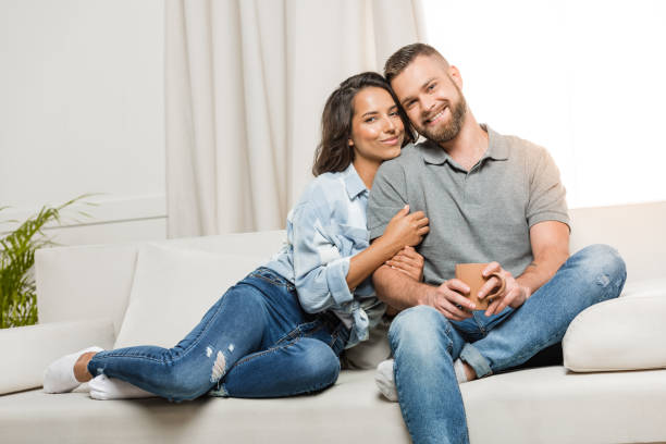 istock young happy couple looking at camera while hugging on sofa at home 811970168