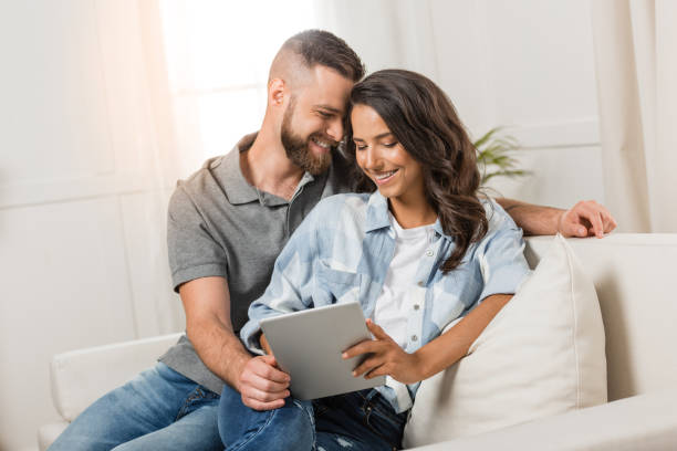 istock tender smiling couple with digital tablet sitting on sofa at home 811970540