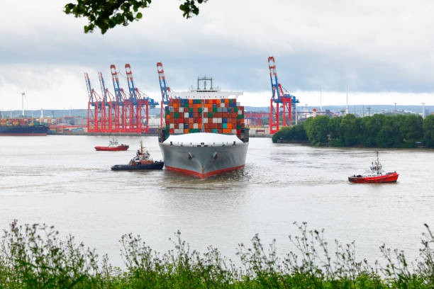Hamburg, Germany - June 24, 2017: Container ship Mackinac Bridge is getting pushed and pulled by two tugboats at the Burchardkai harbor terminal, Hamburg, Germany. View from the Elbchausee close to Övelgönne.