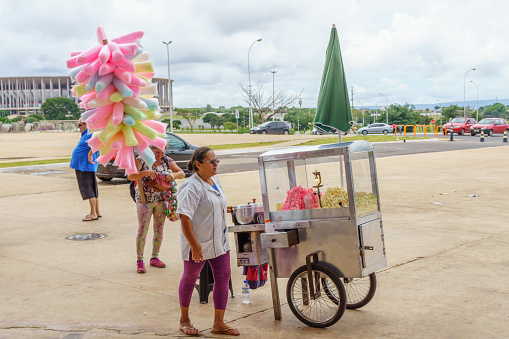 Brasilia, Brazil - February 28, 2017: Working in Brazil businesses theme. Female stallholder selling popcorn from mobile cart. Another is selling cotton candy